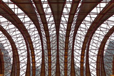 Parlak bir gökyüzüne karşı simetrik kemerli kirişler ve karmaşık kirişler içeren modern mimari çatı yapısının düşük açılı görüntüsü. Londra, İngiltere, 24 Aralık 2023