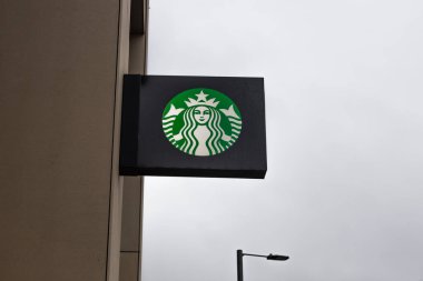 Gri bulutlu gökyüzüne karşı bej bir bina duvarında asılı ikonik Starbucks kahve dükkanı tabelasının dış görünüşü. Londra, İngiltere, 25 Aralık 2023