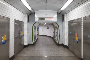 Beyaz fayanslı duvarlar, metal kapılar ve yön tabelasının bulunduğu bir Londra metro istasyonundaki boş yaya tüneli. Londra, İngiltere, 31 Aralık 2023