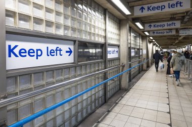 Mavili metro tünelinin perspektif görüntüsü banliyöleri yöneten mavi Keep sol tabelaları. Yoğun bir istasyon koridorunda yürüyen insanlar.