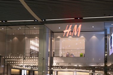 Aydınlatılmış kırmızı logo ve cam cepheli modern bir alışveriş merkezinin H ve M mağaza girişinde. Londra, İngiltere, 10 Şubat 2024