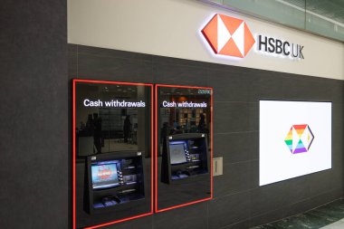 Modern HSBC UK banka şubesinin dış yüzünde iki otomatikleştirilmiş veznedar makinesi ve resmi şirket logosu var. Londra, İngiltere, 17 Şubat 2024