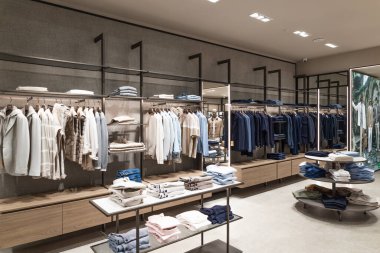 Minimalist bir perakende alanında renklere göre düzenlenmiş gömlek ve ceket raflarının yer aldığı modern bir giyim mağazasının içi. Londra, İngiltere, 17 Şubat 2024