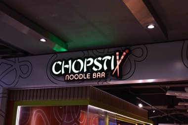Chopstix Noodle Bar 'ın ışıklı tabelasında logoda çapraz çubuklar var. Bir alışveriş merkezinde popüler bir Asya fast food zinciri girişi. Londra, İngiltere, 17 Şubat 2024