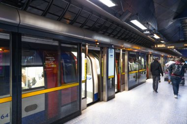 Modern bir Londra metro istasyonunun peronunda yürüyen yolcuların güvenlik cam kapıları ve bir trenleri var. Londra, İngiltere, 17 Şubat 2024