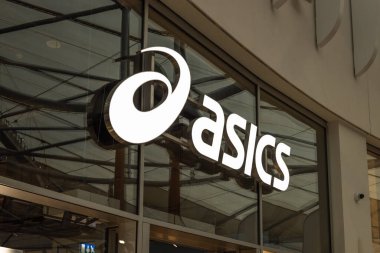 Beyaz Asic logosunun yakın çekimi ve cam bir vitrinde marka ismi. Bir alışveriş bölgesinde modern spor giyim mağazası tabelası. Londra, İngiltere, 17 Şubat 2024