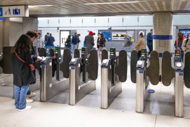 Kalabalık bir metro girişinde otomatik bilet engellerini aşan banliyö görevlileri. Kalabalık saatlerde toplu taşıma için elektronik turnikeleri kullanan insanlar. Londra, İngiltere, 25 Şubat 2024