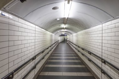 Beyaz kiremitli duvarları ve kavisli tavanı olan boş yeraltı yaya tüneli. Perspektif çizgileri ve parlak ışıklandırması olan metro istasyonunda uzun bir koridor..
