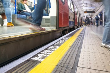 Londra metro peronunun kenarına Gap uyarısı çizilmiş ikonik zihnin düşük açılı görüntüsü ve yoğun saatlerde trene binen bulanık banliyö sakinleri. Londra, İngiltere, 3 Mart 2024