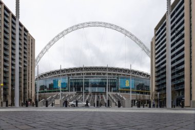 Wembley Stadyumu 'nun geniş bir manzarası ve modern apartman binaları tarafından bulutlu bir gökyüzü altında çerçevelenmiş ana girişi. Londra, İngiltere, 17 Mart 2024