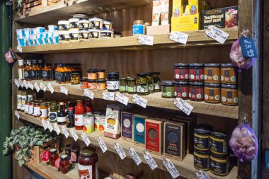 Londra, Borough Market 'teki bir tezgahta bulunan reçel kavanozları, baharatlar ve baharatlar da dahil olmak üzere çeşitli sanatsal gıda ürünleriyle dolu ahşap raflar. Kırsal şarküteri sergisi. Londra, İngiltere, 29 Mart 2024