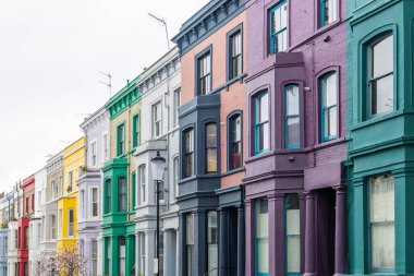 Bir dizi parlak boyanmış Viktorya dönemi teras evleri Notting Hill, Londra 'da bir sokak hizasında, içinde deniz mavisi, mor ve sarı cepheler var..