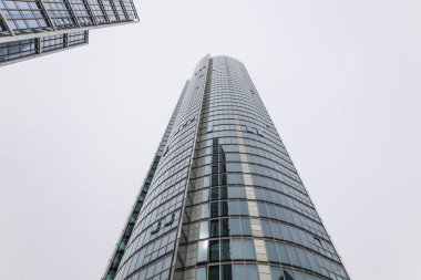 Solucanlar iş bölgesinde bulutlu bir gökyüzüne doğru uzanan eğri büğrü bir cam gökdelenin görüntüsünü izliyorlar..