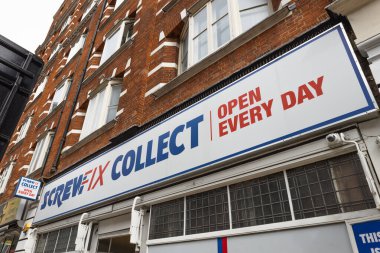 Üzerinde mavi ve kırmızı yazı olan beyaz bir panoda Vida Eki Koleksiyonu Açık yazıyor. Şehir caddesindeki geleneksel tuğla bir binanın önünde. Londra, İngiltere, 6 Nisan 2024