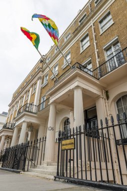 Bolivya ulusal bayrağı ve Wiphala bayrağı Londra caddesindeki elçilik binasının balkonundan beyaz kapılar ve tuğladan duvarlarla dalgalanır. Londra, İngiltere, 6 Nisan 2024
