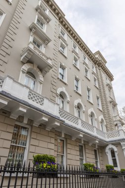 Taştan mimari detaylar, beyaz balkonlar ve gri gökyüzü, Londra, İngiltere 'ye açılan kuşak pencereli büyük Viktorya dönemi ön cephesinin alçak açısı..