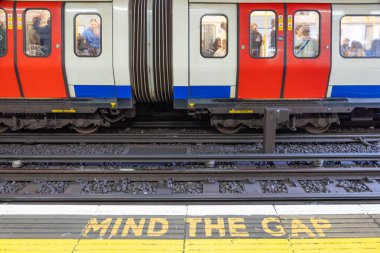 Platformda bir Londra metro treni duruyor. Sarı Zihin Gap uyarısı ile rayların yakınına yazılmış. Londra, İngiltere, 7 Nisan 2024