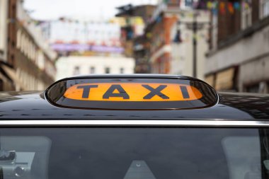 Londra 'da parlak bir şehrin arka planına sahip siyah bir taksinin üstündeki turuncu ışıklı tabelanın yakın görüntüsü..