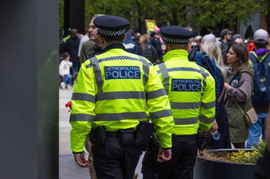 Londra 'da halka açık bir toplantıda kalabalık bir caddede devriye gezen yüksek görüşlü sarı ceketli iki Metropolitan Polisi. Londra, İngiltere, 21 Nisan 2024