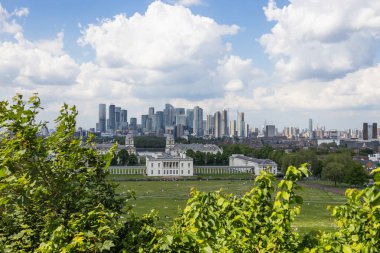 Greenwich Park 'tan Canary Wharf' ın modern gökdelenlerine bakan panoramik bir manzara. Parlak mavi gökyüzü altında beyaz bulutlar. Londra, İngiltere, 19 Mayıs 2024