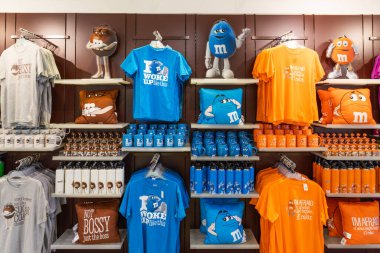 Leicester Meydanı 'ndaki Londra bayrak gemisi mağazasında bulunan tişört, kupa ve yastıklar da dahil olmak üzere resmi M ve M eşyalarıyla dolu renkli raflar. Londra, İngiltere, 2 Haziran 2024