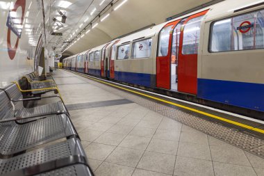 Kırmızı ve mavi bir Londra yeraltı treni, metal koltuklu temiz bir istasyon platformunda durdu. Londra, İngiltere, 2 Haziran 2024