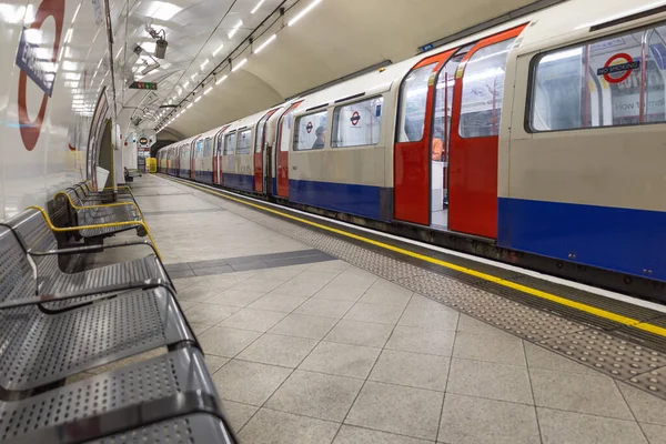 Kırmızı ve mavi bir Londra yeraltı treni, metal koltuklu temiz bir istasyon platformunda durdu. Londra, İngiltere, 2 Haziran 2024