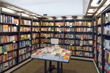 Zeminden tavana kadar çeşitli renkli kitaplarla dolu siyah ahşap raflar ve yeni sürümler için merkezi bir sergi masası olan modern bir kitapçı iç mimarisi. Londra, İngiltere, 8 Haziran 2024