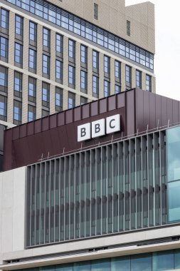 BBC Yayın Merkezi 'nin kurumsal logoyu ve modern yapı malzemelerini vurgulayan düşük açılı görüntüsü. Londra, İngiltere, 22 Haziran 2024