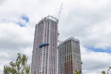 İnşaat sırasında iki yüksek katlı apartmanın alçak açılı görüntüsü ve bulutlu bir gökyüzünün altında bir vinç..