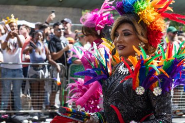 Bir travesti, Londra Onur Yürüyüşü sırasında arka planda kalabalık olan çok renkli bir başlık ve kostüm giyer. Londra, İngiltere, 29 Haziran 2024