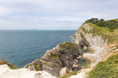 Dorset, İngiltere 'deki Jurassic Sahili' ndeki Lulworth Koyu 'ndaki engebeli beyaz kayalıkların ve turkuaz suların geniş açılı görüntüsü.