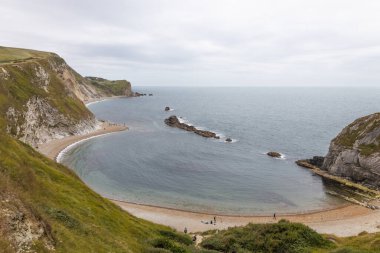 Dorset 'teki at nalı şeklindeki Man OWar Beach' in yüksek açılı manzarası sakin deniz suyu ve dik çimen kayalıklarıyla.