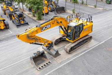 Sarı bir JCB 220X LC sürüngen kazıcısının yüksek açılı görüntüsü diğer ağır makinelerin yanında bir sanayi bölgesine park edilmiş. Londra, İngiltere, 14 Temmuz 2024