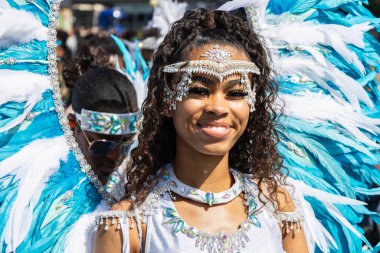 Notting Hill Karnavalı 'nda süslü mavi ve beyaz tüylü bir kostüm giyerken genç bir kadın sıcak bir şekilde gülümsüyor. Londra, İngiltere, 25 Ağustos 2024
