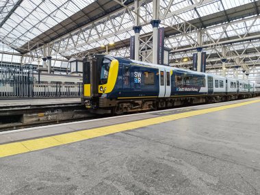 Modern bir Güney Batı Demiryolu treni, büyük, hareketli bir istasyon terminalinde, cam çatı yapısı olan, İngiltere 'de toplu demiryolu ulaşımı sergilenmektedir. Londra, İngiltere, 11 Nisan 2024