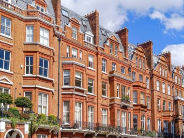 Londra 'daki bir dizi tarihi Viktorya dönemi konağı, açık mavi gökyüzüne karşı geleneksel kırmızı tuğla mimari ve klasik Avrupa tasarım unsurlarını sergiliyor..