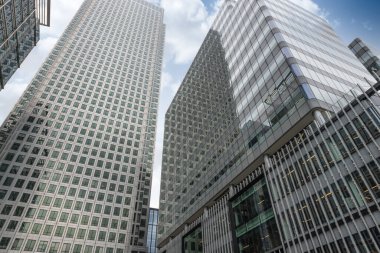 Yoğun bir finans bölgesinde cam cepheli modern gökdelenlerin düşük açılı perspektifi, şehir mimarisi ve kurumsal şehir hayatını gözler önüne seriyor..