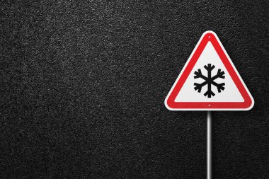 Road sign triangular shape with a picture of snowflakes on a background of asphalt. The texture of the tarmac, top view. clipart