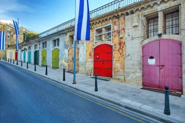 Gece renklerinde Antik Valletta. Limanın yanındaki sokakta çok renkli kapılar, Malta bayrağı. İnsan yok. Kartpostal Malta 'da tatiller.