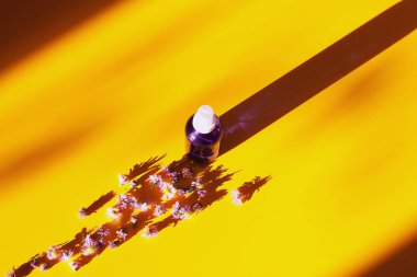 Sarı arka planda çiçekler olan mor sıvı kozmetik şişesi. Düz yat, boşluğu kopyala