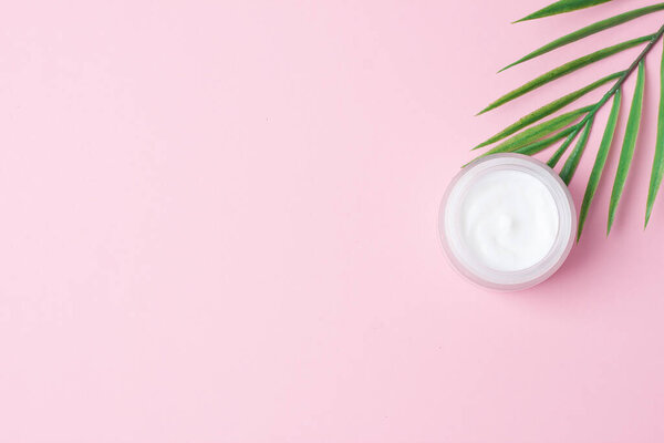 Jar of cosmetic cream with leaf palm branch on pink background. Flat lay, copy space