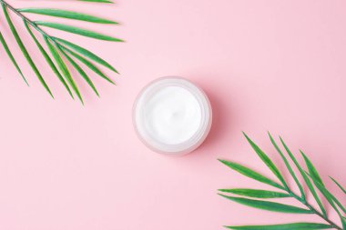 Pembe arka planda yaprak palmiye dalı olan kozmetik kremi kavanozu. Düz yat, boşluğu kopyala