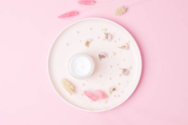 Pembe arka planda kuru çiçekli bir kavanoz kozmetik kremi.
