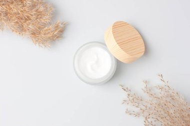 Beyaz arka planda otla kaplı bir kavanoz kozmetik kremi. Düz yat, boşluğu kopyala