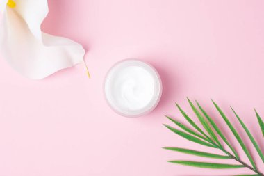 Kavanozda palmiye yaprağı ve pembe arka planda beyaz çiçek olan kozmetik kremi. Düz yatıyordu