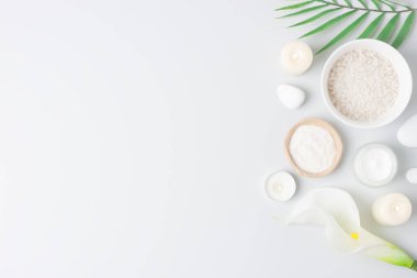 Bir kase tuz, cilt bakım ürünleri, beyaz taşlar, mumlar, palmiye yaprağı ve beyaz çiçekli bir kaplıca. Düz yat, boşluğu kopyala