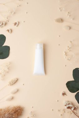 Beyaz bir kozmetik krem tüpü ve pastel bej arka planda çiçekler. Düz yat, boşluğu kopyala