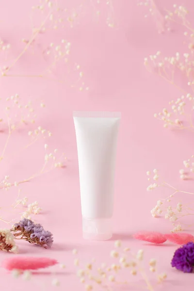 White tube of cosmetic cream with flowers on pink background. Flat lay, copy space