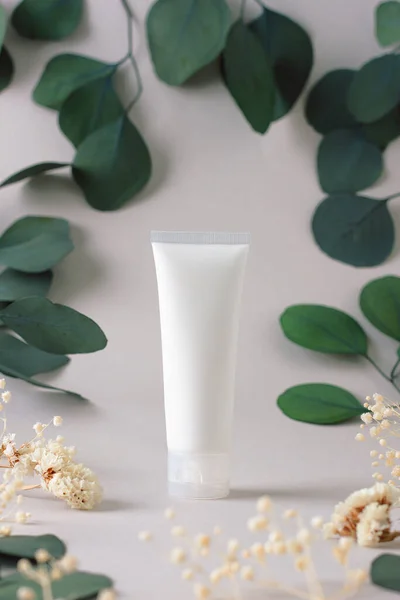White tube of cosmetic cream with flowers and green leaves on grey background. Close up